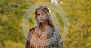 Smiling Caucasian woman with deep gaze standing on background of yellow leaves and looking at camera. Pretty woman in