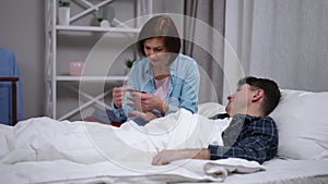 Smiling Caucasian woman filing nails for ill man lying in bed talking. Portrait of caring wife enjoying leisure with