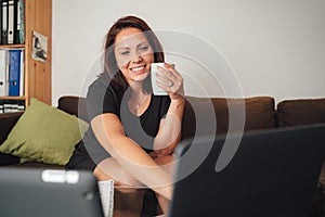 Smiling Caucasian woman having coffee while using laptop in living room at home