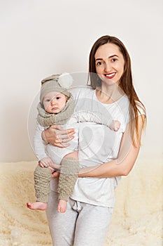 A smiling Caucasian woman holds an eight-month-old baby girl at home. knitted leggings, Snood and cap