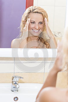 Smiling Caucasian Woman Looking At Mirror's Reflection and Examining Her Face and Hair.