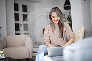 Smiling caucasian woman sitting in an armchair at home and using laptop