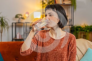 Smiling Caucasian woman sitting at home leading healthy lifestyle, drinking a glass of pure water