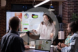 Smiling caucasian woman in startup office doing business presentation on big tv screen with charts