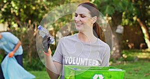 Smiling caucasian woman wearing volunteer t shirt holding recycling crate, collecting plastic waste