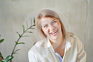 Smiling caucasian young adult woman in white shirt with plant background indoors photo