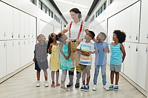 Smiling caucasian young female teacher with african american elementary school students in corridor