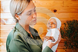 Smiling caucasian young woman holding newborn african american baby doll in arms and looking at her, indoors.