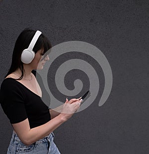 Smiling caucasian young woman listening to rock band singer music song e-book podcast in headphones choosing audio track on mobile