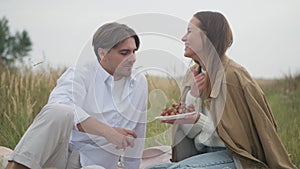 Smiling charming woman feeding man with grapes eating fruit in slow motion. Portrait of happy carefree relaxed Caucasian