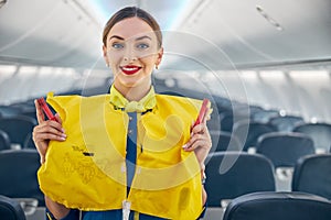 Smiling cheerful air hostess wearing life jacket on her shoulder