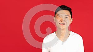 Asian young man's portrait on red studio background. Concept of human emotions, facial expression, youth, sales, ad.