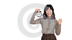 Smiling cheerful attractive young asian woman wearing sweater shirt holding alarm clock showing fist up looking camera isolated on