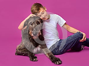 Smiling cheerful eleven years teen in white t-shirt and jeans with brown big dog on fuchsia color background in photo studio.