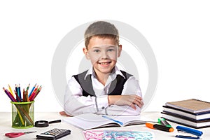Smiling cheerful excellent pupil sitting still at the desk with white background