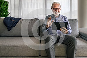Smiling cheerful happy senior man waving and gesturing to camera having online video call on hand held tablet portable device