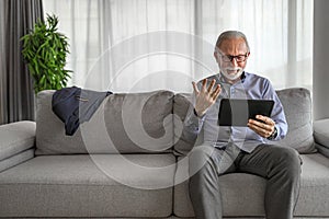 Smiling cheerful happy senior man waving and gesturing to camera having online video call on hand held tablet portable device