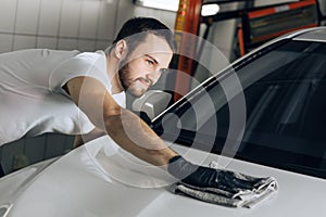 Smiling cheerful mechanic wasing and polishing a car surface