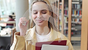 Smiling cheerful teen girl student walking in university library, portrait.