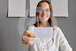 Smiling cheerful woman nurse holding empty business or visit card offering her medical services doctor wearing white lab coat and