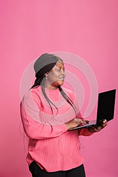 Smiling cheerful woman with pink t-shirt holding laptop computer studying for univerisity