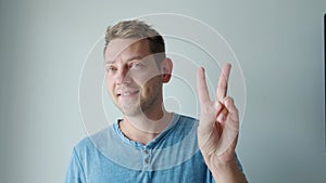 Smiling cheerful young man showing two fingers up greeting gesture, victory sign. Body language, success, luck