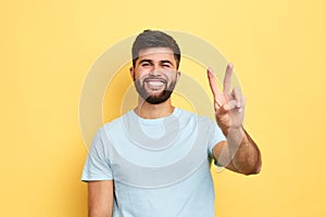 Smiling cheerful young man showing two fingers up, victory sign