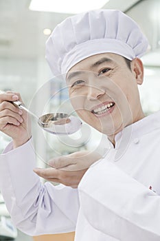 Smiling chef with spoon lifted to his mouth, tasting food, portrait