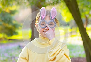 smiling cherful little girl in glasses with rabbit ears in garden. Easter bunny funny costume photo