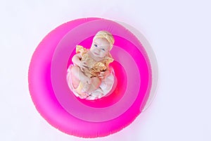 A smiling child in a bathing suit with a pink swimming ring lies on a white isolated background. Holidays at sea with baby,