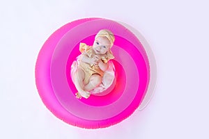A smiling child in a bathing suit with a pink swimming ring lies on a white isolated background. Holidays at sea with baby,