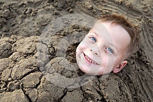 Smiling child buried in sand on beach