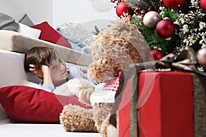Smiling child and the Christmas tree decorated with balls, in the living room next to the teddy bear gift