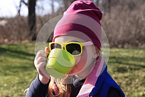 Smiling child in colorful clothes drinks tea from bright green reusable cup Spring nature background Eco-friendly picnic