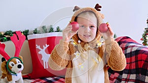 Smiling child in deer costume looking into the camera making funny face with red Christmas balls on her eyes.