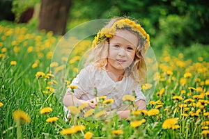 Smiling child girl in dandelion wreath on spring flower field