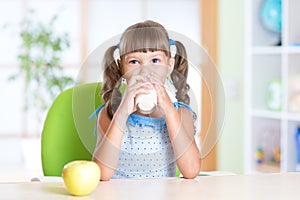 Smiling child girl drinking milk from glass at
