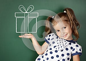 Smiling child girl hold drawn gift box near school blackboard