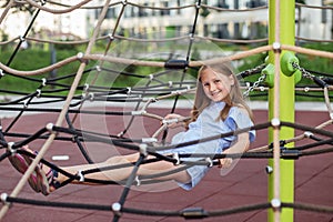 Smiling child girl lying on rope net playground
