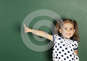 Smiling child girl show with a finger blank school blackboard, c