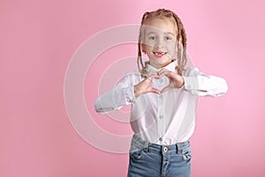 Smiling child girl showing heart sign on pink background. Kid making heart shape gesture with hands, Valentine day