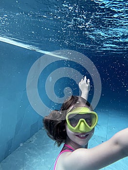 Smiling child in goggles swim, dive in the pool with fun - jump deep down underwater. Healthy lifestyle, people water