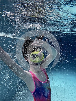 Smiling child in goggles swim, dive in the pool with fun - jump deep down underwater. Healthy lifestyle, people water