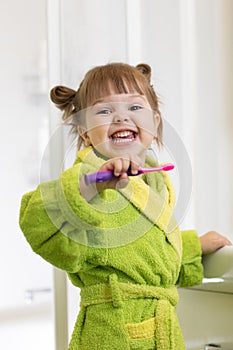 Smiling little girl brushing teeth in bathroom