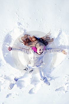 Smiling child lying on snow with copy space. Funny kid making snow angel. Child girl playing and making a snow angel in