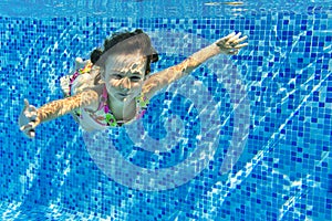 Smiling child swims underwater in pool