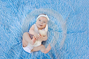 A smiling child in a white bodysuit lies on a blue fur background with a toy
