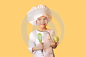 Smiling child in white chef uniform,holding a cabbage and a whisk in his hands. Cheerful yellow background