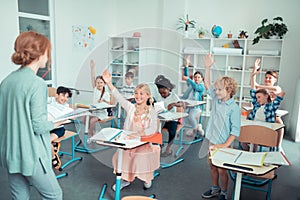 Smiling children in a classroom interacting with the teacher.