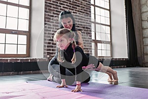 Smiling children gym trainer working with a little girl showing how to do plank exercise in fitness studio